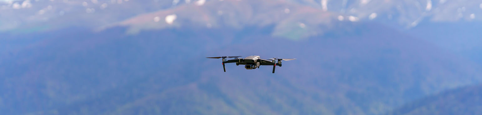Black drone flying over a forested mountain.