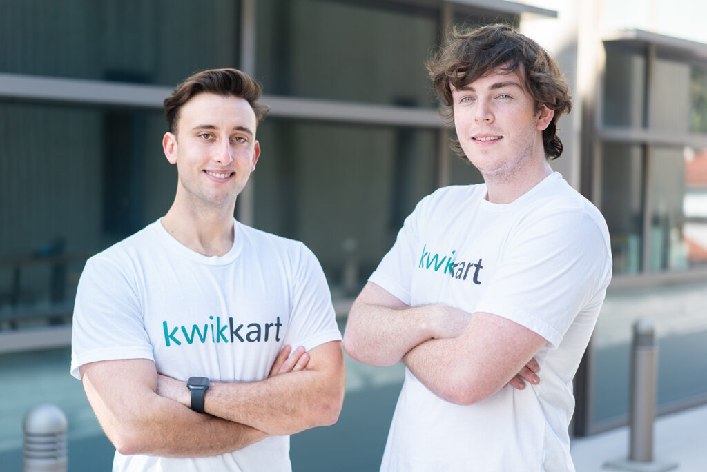 Two people wearing t-shirts that read "kwikkart" stand in front of a building.