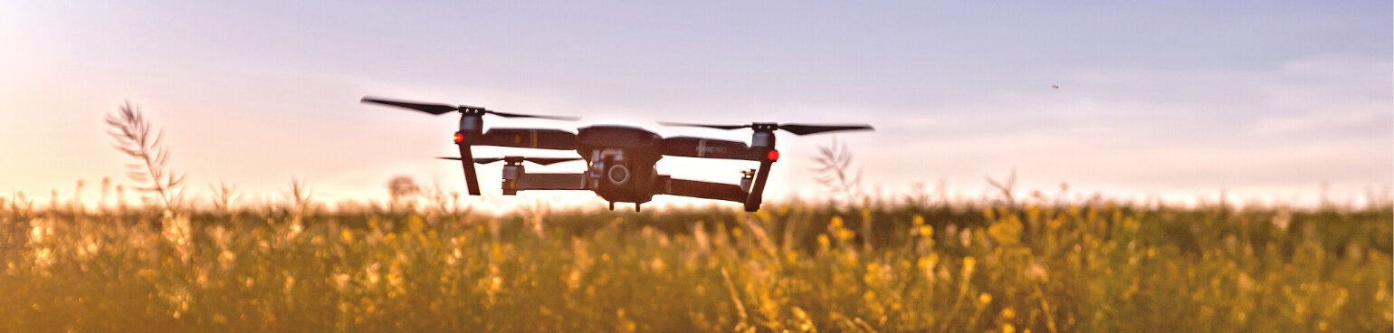 A drone flying over a grassy field at sunset.