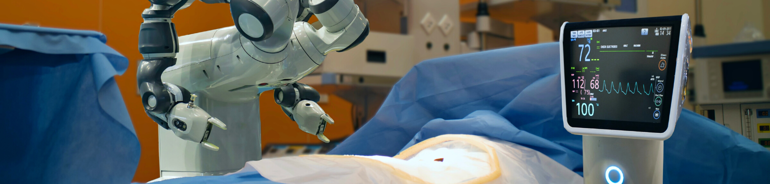 Close crop of a robotic arm and a heart monitor screen next to a form covered by blue surgical drapes.